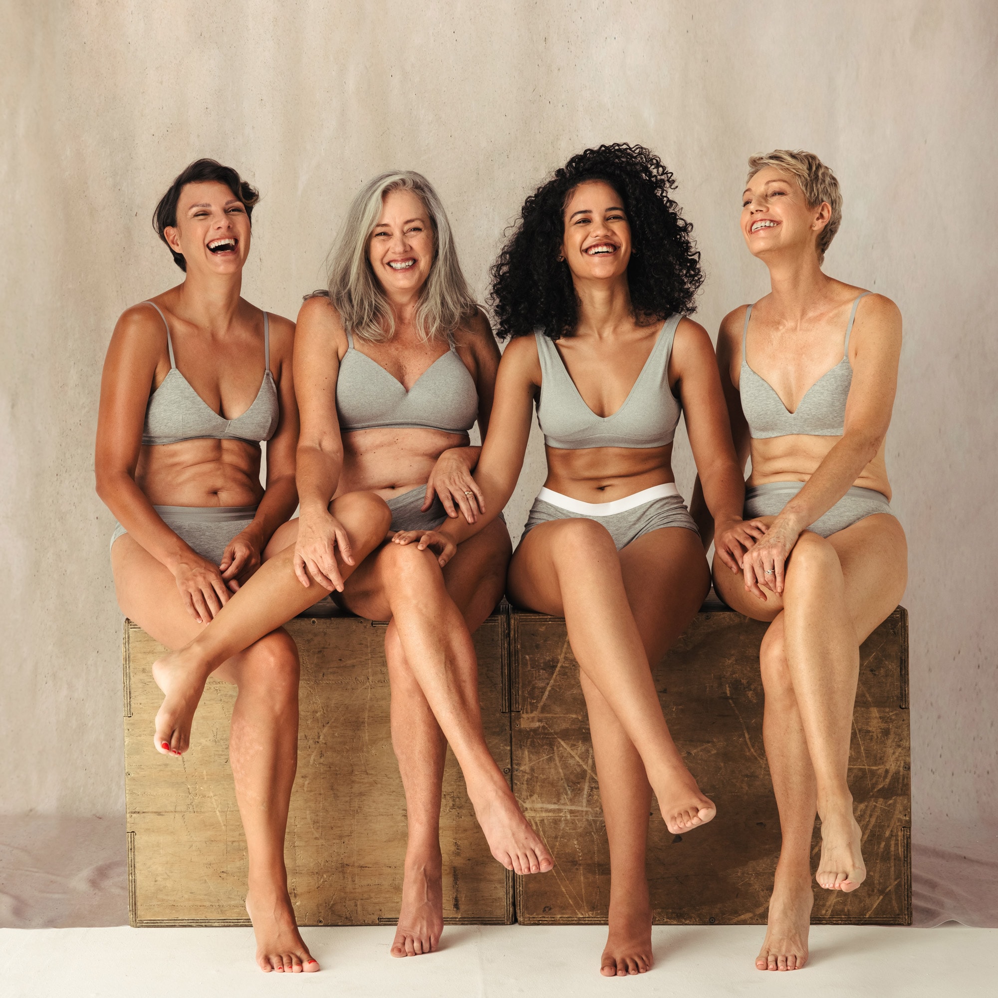 Four women in grey undergarments sitting and smiling