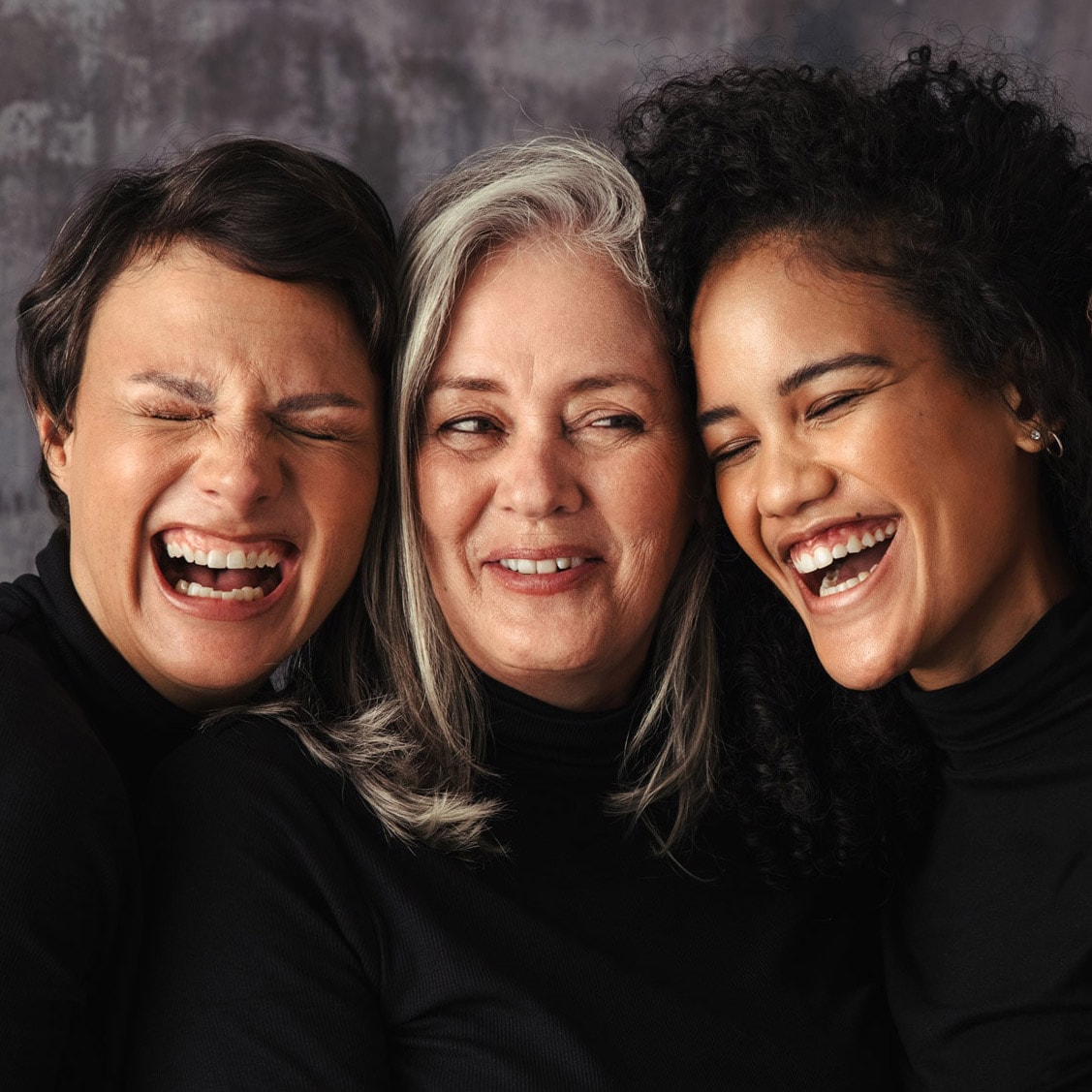 Four women in black turtlenecks laughing