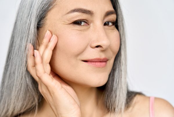 Woman with long grey hair touching her face