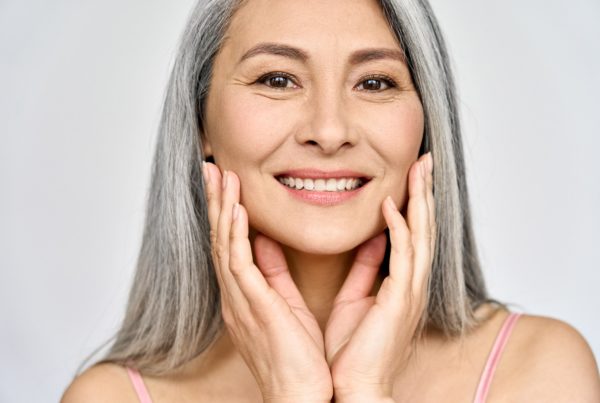 Woman with long grey hair smiling and touching her face